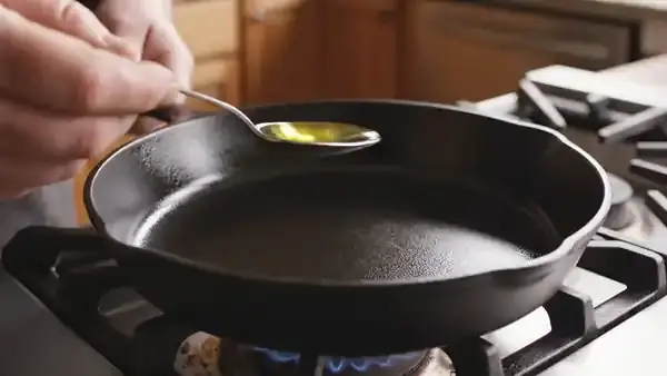 A tablespoon of cooking oil poured into a cast-iron skillet on a stove