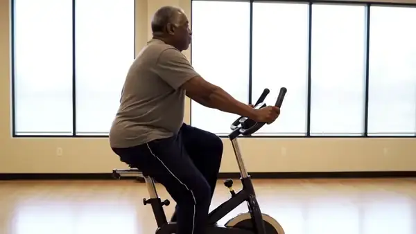 A man in his late sixties pedaling a stationary exercise bike at an easy pace, seen from the side